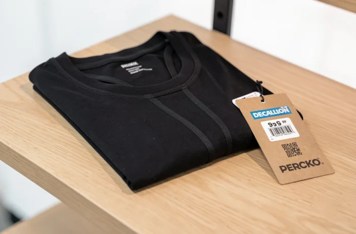 Camiseta Percko preta dobrada com etiqueta de preço Decathlon sobre uma superfície de madeira clara, vista de cima do produto